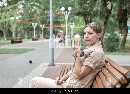 Frau sitzt auf der Bank im Park und isst Eis Stockfoto