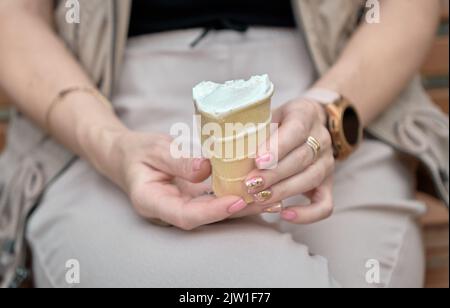 Damenhänden mit Eiscreme im Waffelbecher. Stockfoto
