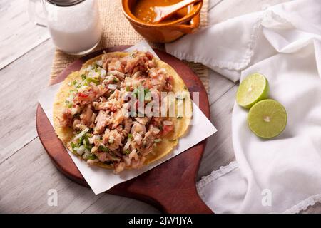 Taco de Carnitas. Maismehl-Tortilla mit frittiertem Schweinefleisch. Traditionelle mexikanische Vorspeise, begleitet von Koriander, Zwiebel und heißer Sauce. Stockfoto