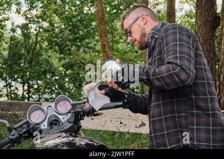 Mann Biker mittleren Alters Motorradfahrer Reinigung eines Motorrads auf der Seite der Straße im Wald Stockfoto