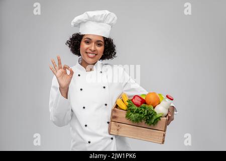 Glückliche lächelnde Köchin mit Essen in Holzkiste Stockfoto