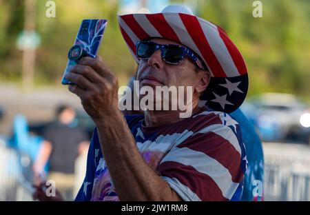 Wilkes Barre Township, Vereinigte Staaten. 02. September 2022. Ein Mann, der in Rot, Weiß und Blau gekleidet ist und sich „vordere Reihe Joe“ nennt, benutzt sein Mobiltelefon. Am Tag, bevor Präsident Trump bei einer Kundgebung in Wilkes-Barre sprechen soll, haben Händler aus dem ganzen Land entlang der Straße Geschäfte eingerichtet, um Waren zu verkaufen. Andere haben in der Arena gezeltet, um „First Row Joe's“ zu sein, um Karten für die Rallye zu bekommen, sobald sie können. (Foto von Aimee Dilger/ SOPA Images/Sipa USA) Quelle: SIPA USA/Alamy Live News Stockfoto