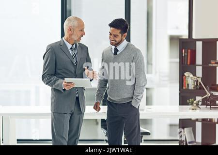 Diese Zahlen sehen gut aus. Zwei Geschäftsleute, die in ihrem Büro ein digitales Tablet betrachten. Stockfoto