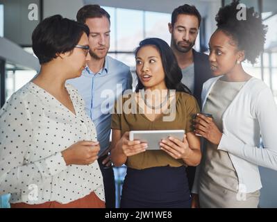 Ich kann Ihnen zeigen... eine Gruppe von Geschäftsleuten, die im Büro ein Tablet betrachten. Stockfoto