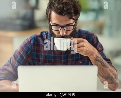 Ein Schluck Kaffee tut Wunder für meine Kreativität. Ein Designer, der Kaffee trinkt, während er an seinem Laptop arbeitet. Stockfoto