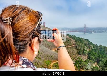 Eine Dame fotografiert die Golden Gate Bridge auf ihrem Handy während ihres Urlaubs in San Francisco, Kalifornien, USA Stockfoto