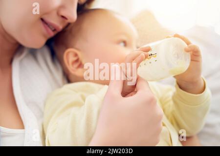 HES meine Definition von perfekt. Ein Baby, das seine Flasche trinkt, während es in den Armen seiner Mutter liegt. Stockfoto