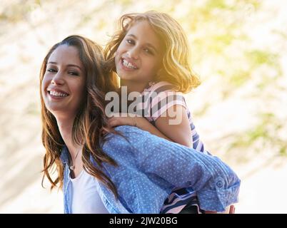 Unsere gemeinsame Zeit ist das größte Geschenk. Eine Mutter gibt ihrer Tochter eine Huckepack-Fahrt. Stockfoto