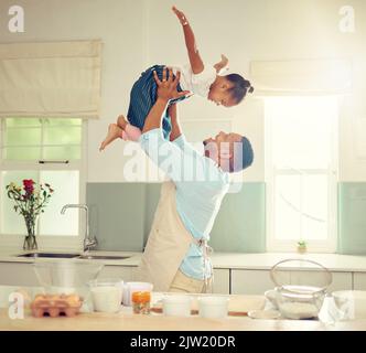 Glücklicher schwarzer Vater und Tochter, die in einer Küche spielen, während sie zusammen kochen, sich verkleben und lachen. Afroamerikanische Eltern genießen die Zeit mit der Familie Stockfoto