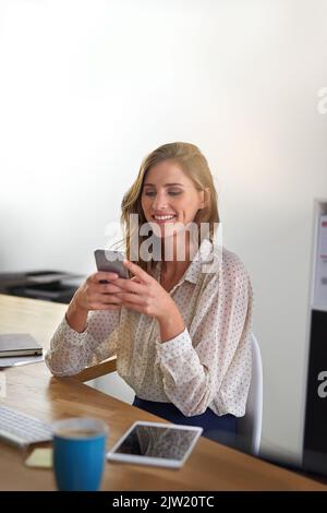 Treffen wir uns nach der Arbeit. Eine junge Geschäftsfrau, die im Büro ein Mobiltelefon benutzt. Stockfoto