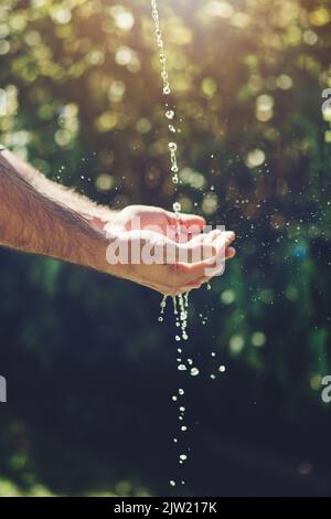 Bleib auf der kühlen Seite. Nahaufnahme eines Mannes, der seine Hände unter einem Wasserstrom im Freien hält. Stockfoto