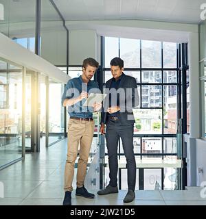 Daten und Fakten synchronisieren: Zwei Kollegen sprechen über ein digitales Tablet, während sie in einem modernen Büro stehen. Stockfoto