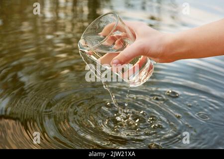 Seid wasserklug. Wasser wird aus einem Glas in einen Teich gegossen. Stockfoto