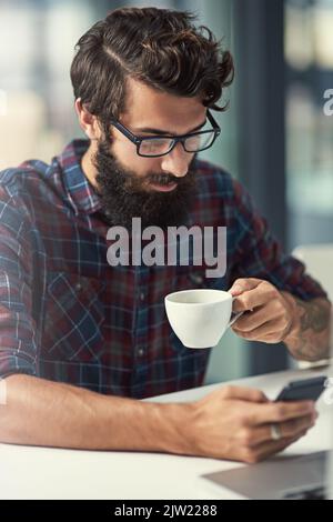 Eine Social-Media-Präsenz ist wichtig für seinen Job. Ein junger Designer hat Kaffee, während er sein Handy benutzt. Stockfoto