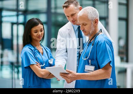 Für den schnellen Zugriff auf alle Patientenberichte. Eine Gruppe von Ärzten, die in einem Krankenhaus an einem digitalen Tablet arbeiten. Stockfoto