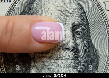 Der Finger einer Frau liegt auf hundert Dollar und verschließt ihr die Augen vor Benjamin Franklin, Finanzen und Wirtschaft, einer Frau auf Geld Stockfoto