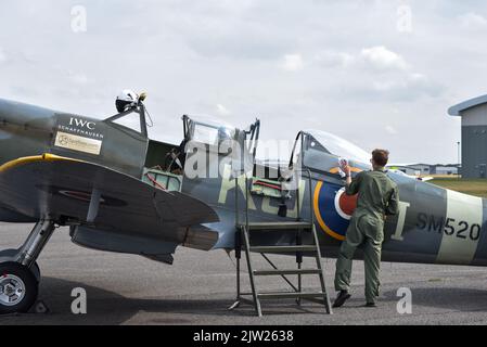 SM250 zweisitzige Spitfire, die zwischen den Flügen auf der Start- und Landebahn des Flughafens Solent geparkt wurde. Ein Crew-Mitglied reinigt das Glas. Stockfoto