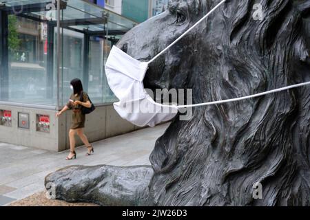 Tokio, Japan. 24. August 2022. Eine Frau mit Gesichtsmaske kommt am Samstag an einer Löwenstatue mit Gesichtsmaske, dem Maskottchen des Kaufhauses Mitsukoshi im Tokioter Modeviertel Ginza, vorbei. Kredit: SOPA Images Limited/Alamy Live Nachrichten Stockfoto