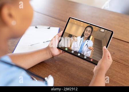 Lächelnde asiatische Ärztin, die während eines Videoanrufs mit einer afroamerikanischen Kollegin gestikuliert Stockfoto