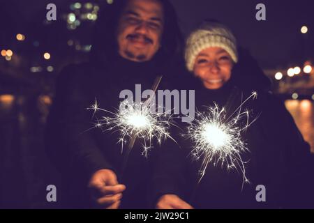 Paar mit Wunderkerzen in der Nacht. Glückliche Menschen genießen Feuerwerk im Freien Stockfoto