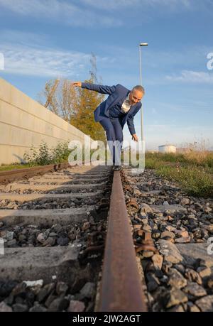 Betrunkener Mann im Anzug balanciert über Bahngleise am Hafen, Rheinhafen, Karlsruhe Stockfoto