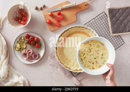 Von oben anonyme Frau, die Schüssel mit rohen Eiern mit Milch und Gemüse in der Nähe von leerer Kruste trägt, während sie Quiche zum Mittagessen in der Küche zu Hause kocht Stockfoto