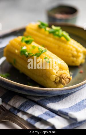 Nahaufnahme von gekochtem Mais mit Salz und grünen Zwiebeln auf grauem Hintergrund Stockfoto