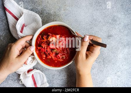 Draufsicht Ernteguthände mit ukrainischem roten Beetroot-Borscht, serviert in der Schüssel auf rustikalem Hintergrund Stockfoto