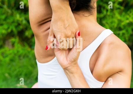 Rückansicht einer anonymen aktiven Frau, die beim Yoga-Training im Park mit grünen Bäumen die Hände hinter dem Rücken verriegeln lässt Stockfoto