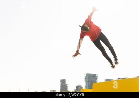 Der Mann springt vom Gebäuderand und zeigt einen Salto, während er an sonnigen Tagen in der Stadt parkour Stockfoto