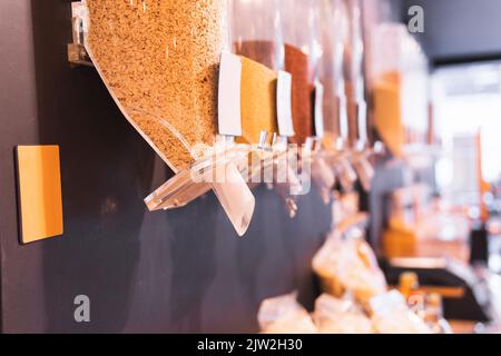 Kunststoffspender mit verschiedenen Körnern, die an der Wand in einem umweltfreundlichen Lebensmittelgeschäft hängen Stockfoto