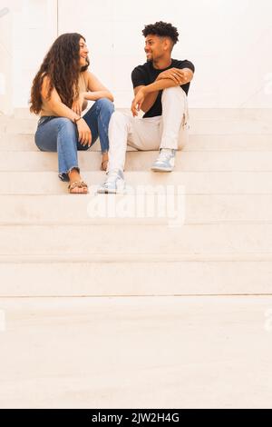 Ein junges, lächelndes Paar, das auf einer Treppe sitzt und redet Stockfoto