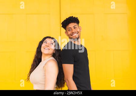 Porträt eines selbstbewussten jungen Paares, das sich gegen eine gelbe Tür zurücklehnen kann Stockfoto