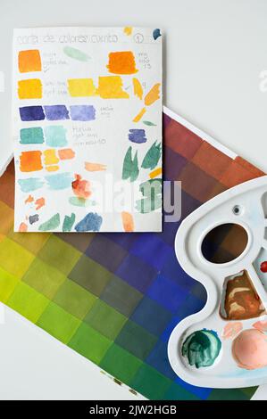 Ansicht von oben auf Kunststoffpalette mit Farbe und Papierblättern mit Farbschemen auf weißem Schreibtisch im Studio Stockfoto