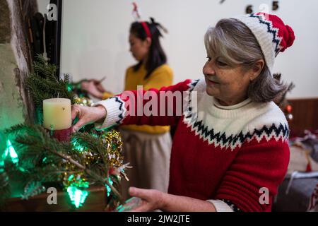 Fröhliche multirassische Frau Dekoration Kamin mit TV während der Weihnachtsferien im hellen Raum zu Hause Stockfoto