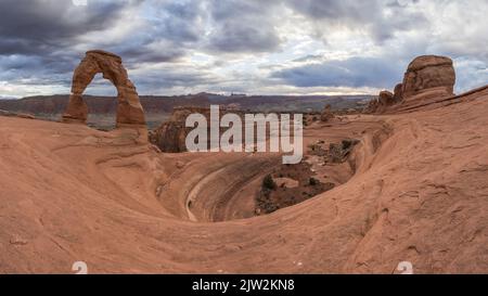 Atemberaubende Aussicht auf Delicate Arch in der Nähe des rauen Canyons gegen den wolkigen Sonnenuntergang im Arches National Park in Utah, USA Stockfoto