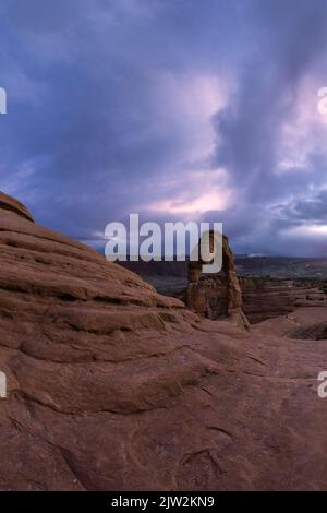 Atemberaubende Aussicht auf Delicate Arch in der Nähe des rauen Canyons gegen den wolkigen Sonnenuntergang im Arches National Park in Utah, USA Stockfoto