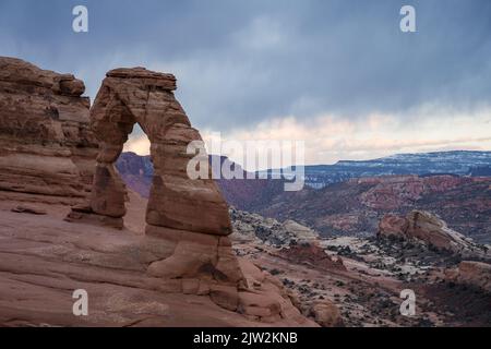 Atemberaubende Aussicht auf Delicate Arch in der Nähe des rauen Canyons gegen den wolkigen Sonnenuntergang im Arches National Park in Utah, USA Stockfoto