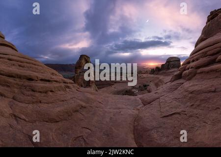 Atemberaubende Aussicht auf Delicate Arch in der Nähe des rauen Canyons gegen den wolkigen Sonnenuntergang im Arches National Park in Utah, USA Stockfoto