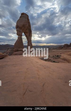 Atemberaubende Aussicht auf Delicate Arch in der Nähe des rauen Canyons gegen den wolkigen Sonnenuntergang im Arches National Park in Utah, USA Stockfoto