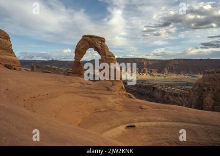 Atemberaubende Aussicht auf Delicate Arch in der Nähe des rauen Canyons gegen den wolkigen Sonnenuntergang im Arches National Park in Utah, USA Stockfoto