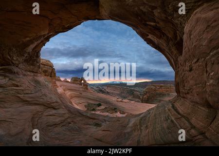 Atemberaubende Aussicht auf Delicate Arch in der Nähe des rauen Canyons gegen den wolkigen Sonnenuntergang im Arches National Park in Utah, USA Stockfoto