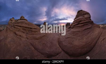 Atemberaubende Aussicht auf Delicate Arch in der Nähe einer rauen Schlucht gegen bewölkten Himmel mit Mond im Arches National Park in Utah, USA Stockfoto