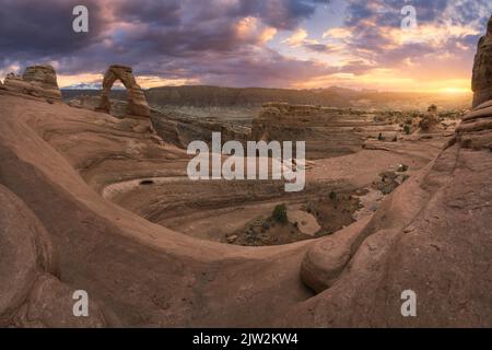 Atemberaubende Aussicht auf Delicate Arch in der Nähe des rauen Canyons gegen den wolkigen Sonnenuntergang im Arches National Park in Utah, USA Stockfoto
