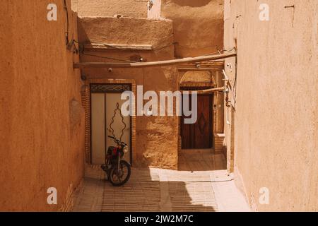 Motorrad geparkt in der Nähe der schäbigen Wand eines alten Steinhauses in der historischen Stadt mit engen Straßen und Holztüren an sonnigen Tag im Iran Stockfoto