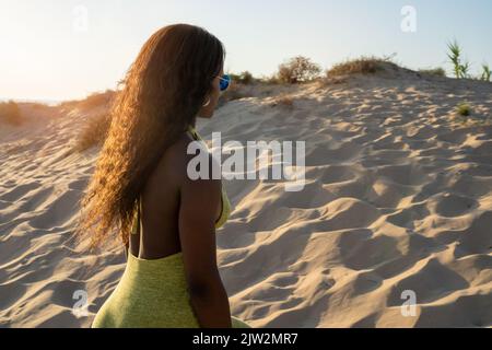 Seitenansicht afroamerikanische Touristen in stilvoller Kleidung, die am Sommertag am Strand am Sandstrand spazieren gehen Stockfoto