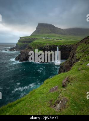Lange Exposition von Meerwasser plätschern in der Nähe von rauen Klippen gegen bewölkten Sonnenaufgangshimmel in stürmischen Morgen auf den Färöer-Inseln Stockfoto