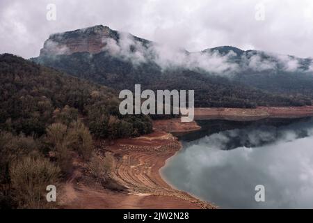 Drohnenansicht des mit grauen Wolken bedeckten Bergrückens am Ufer des ruhigen Flusses mit reflektierendem Wasser in der Natur Stockfoto