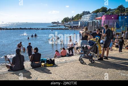 Die Menschen sitzen in der Sonne am Rande der drei Muscheln Lagune an der Küste in Southend-on-Sea, Essex, Großbritannien. Stockfoto