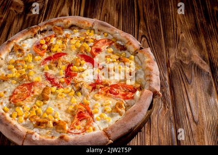 Pizza für Kinder auf Sahnebasis mit Hühnerfilet, Tomaten, Mais und Mozzarella-Käse auf Holzhintergrund. Stockfoto